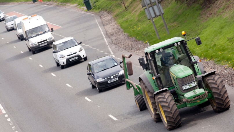 Queue of traffic behind a slow moving vehicle farming tractor on the A75 road UK