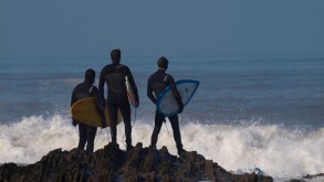 Surfers standing on rocks looking out to sea, Westward Ho!, Devon, UK