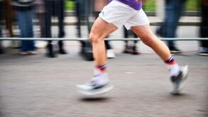 Close-up shot of runner's legs in motion, showing powerful stride as race down street, with blurred spectators in background emphasizing speed and intensity of moment.