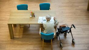 ALMELO, THE NETHERLANDS - JUNE 14, 2016: An elderly woman is reading a newspaper on the table of an elderly home.