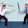 Photo of two businessmen having a sword fight using umbrellas, good image to convey conflict, rivalry or disagreement.