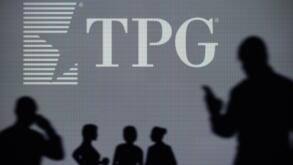 The TPG Capital logo is seen on an LED screen in the background while a silhouetted person uses a smartphone (Editorial use only)