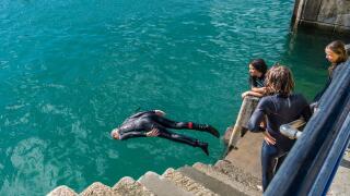Young teenagers diving into the sea at high tide from the quay in Newquay Harbour in Cornwall in the UK.