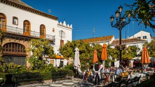 NOVEMBER 21, 2017 - MARBELLA, SPAIN. People having lunch outside in a public plaza on a sunny day. Traditional white buildings.