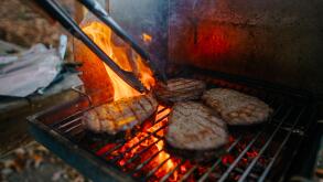 four well-done ribeye-steaks with high flames and barbecue tong on the grill