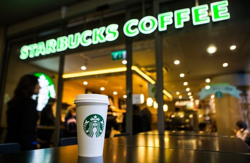 A Starbucks coffee cup sitting on a table outside Starbucks coffee shop, Canary Wharf. London, UK.