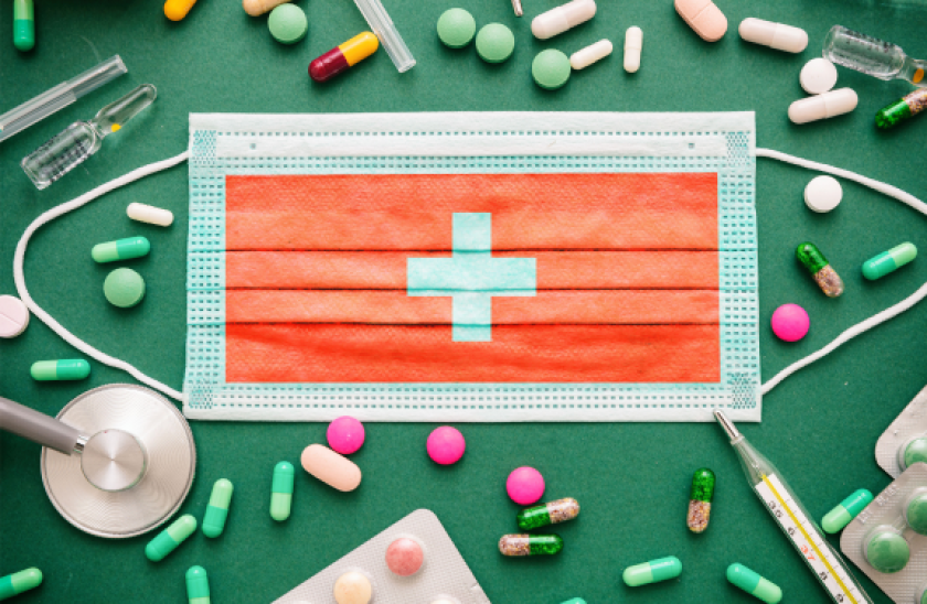 Surgical mask with Swiss flag design, surrounded by pills, on a green surface