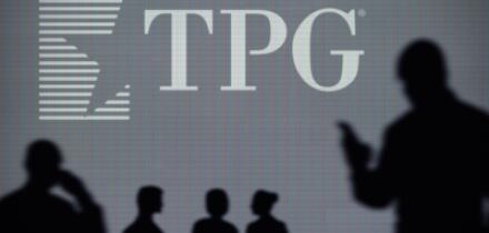 The TPG Capital logo is seen on an LED screen in the background while a silhouetted person uses a smartphone (Editorial use only)