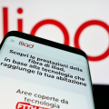 Mobile phone with website of telecommunications company Iliad Italia S.p.A. in front of business logo. Focus on top-left of phone display.