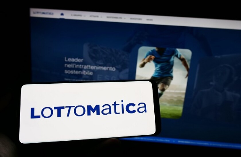 Person holding cellphone with logo of Italian gambling company Lottomatica SpA on screen in front of business webpage. Focus on phone display.