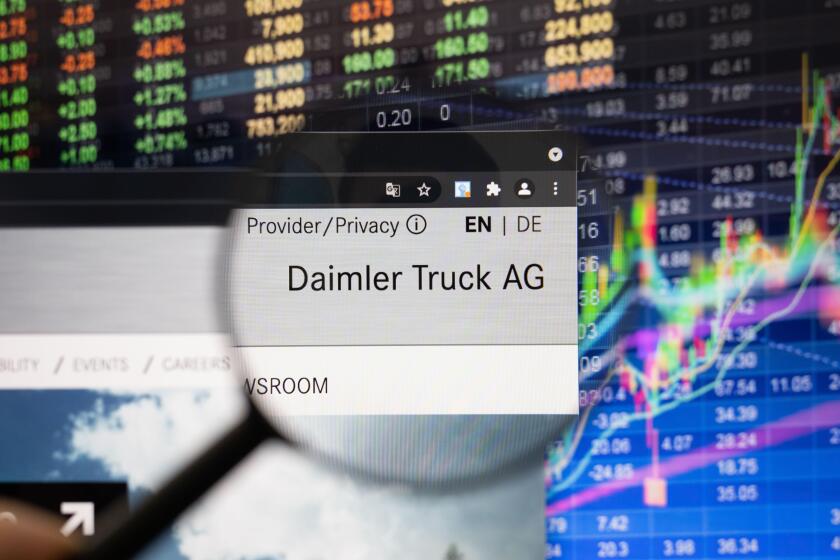 Daimler Truck AG company logo on a website with blurry stock market developments in the background, seen on a computer screen