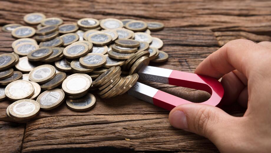 Cropped image of businessman's hand pulling coins with magnet on wooden table