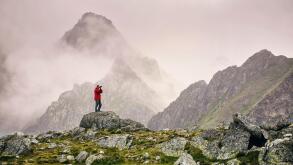 Hiker with camera standing on top of a mountain