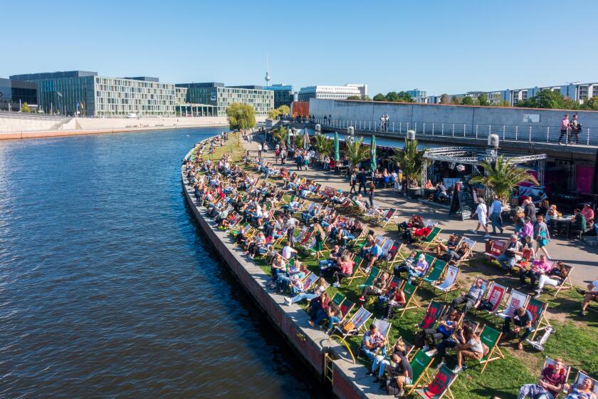 People sunbathing on deckchairs by Spree river on Capital Beach in central Berlin, summer. Image shot 08/2023. Exact date unknown.