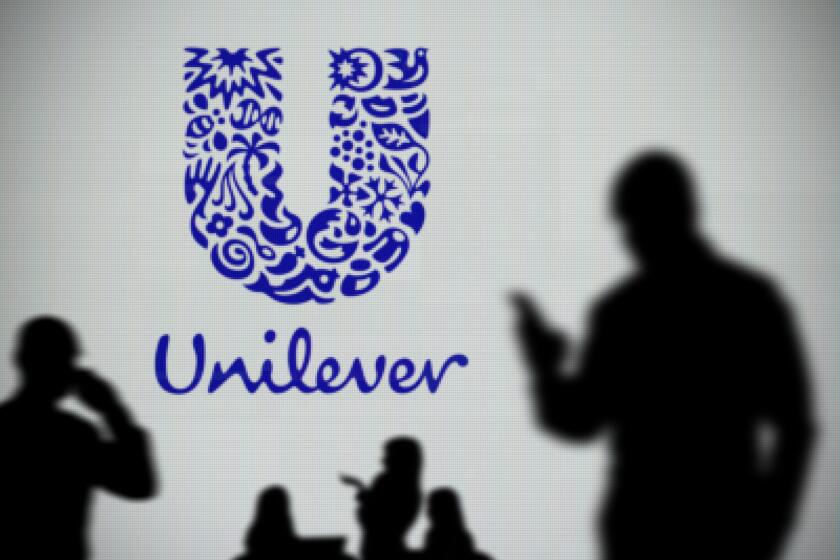 The Unilever logo is seen on an LED screen in the background while a silhouetted person uses a smartphone in the foreground (Editorial use only)