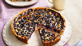 Blueberry cream cheese tart with slice cut away, cake server, coffee cup and separate slice on plate nearby