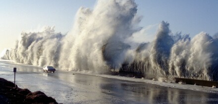 A huge storm surge wave dwarfs a car travelling on Highway 1 at Solimar Beach California