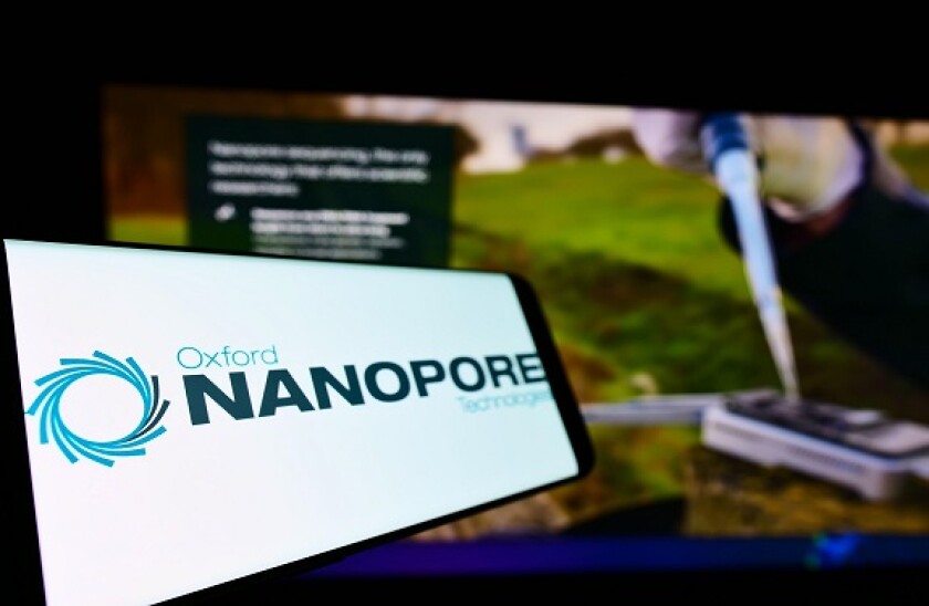 Cellphone with logo of company Oxford Nanopore Technologies Limited on screen in front of business webpage. Focus on left of phone display.