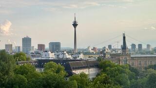 Dusseldorf skyline with Rheinturm tower, modern architecture, and the Rhine under a dramatic cloudy sky.
