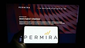 Person holding smartphone with logo of British investment company Permira Holdings Limited on screen in front of website. Focus on phone display.