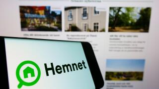 Mobile phone with logo of Swedish property platform company Hemnet AB on screen in front of business website. Focus on center-left of phone display.