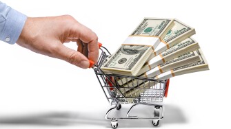 Businessman's hand holds grocery cart full of money stacks