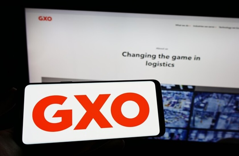 Person holding smartphone with logo of US supply chain company GXO Logistics Inc. on screen in front of website. Focus on phone display.