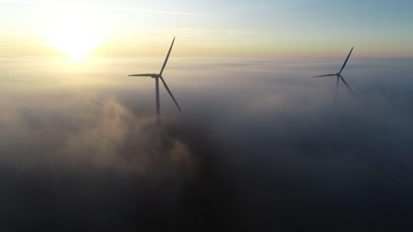 Aerial photo of wind turbines at sunrise with low clouds / fog covering the ground.