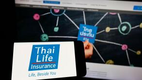 Person holding smartphone with logo of company Thai Life Insurance Public Co. Ltd. on screen in front of website. Focus on phone display.