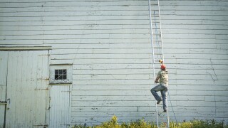 New York state USA man climbing ladder propped against clapboard barn