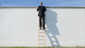 Businessman on ladder looking over wall
