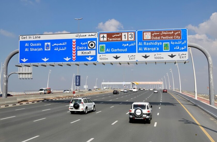 Dubai cars & traffic driving along seven lane motorway & gantry blue sign leading to airport terminals 1 & 3 United Arab Emirates UAE Middle East