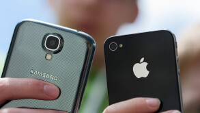 Two teenagers are posing with their Samsung Galaxy S4 (left) and iPhone 4 smartphones.