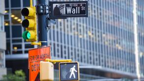 Wall street sign in the foreground and a huge blurred building in the background in Manhattan.