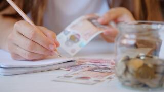 coins jar,New Plastic Ten and twenty Pound note sterling in woman hands making notes in notebook. Crisis and saving concept. British finance money sis