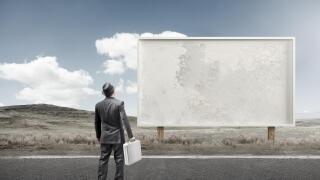 A business man standing and staring at a blank billboard advertisement.