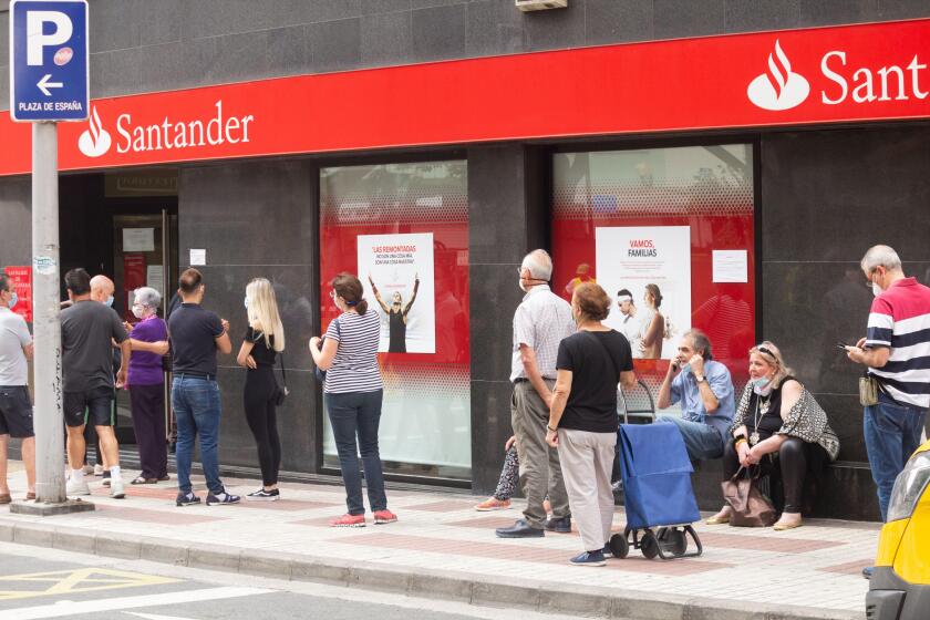 People wearing face masks queuing outside Santander bank during Covid 19, Coronavirus pandemic in Spain