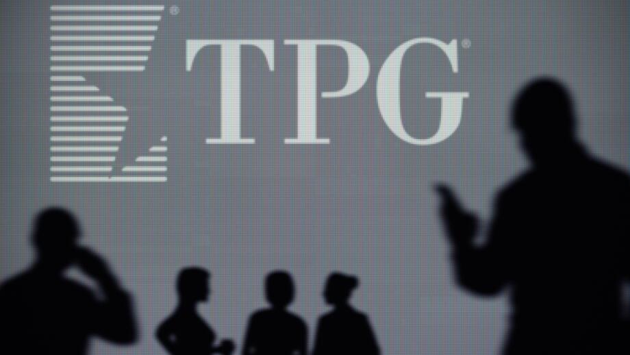 The TPG Capital logo is seen on an LED screen in the background while a silhouetted person uses a smartphone (Editorial use only)