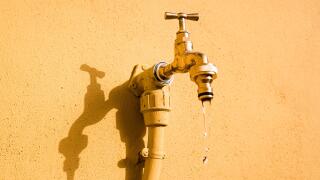 A wall tap on a wall in the sun from which fresh water drips.