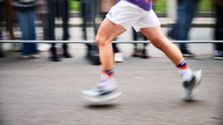 Close-up shot of runner's legs in motion, showing powerful stride as race down street, with blurred spectators in background emphasizing speed and intensity of moment.