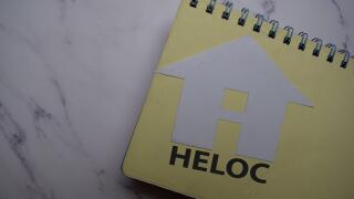 HELOC write on sticky note and house made from paper isolated on Office Desk.