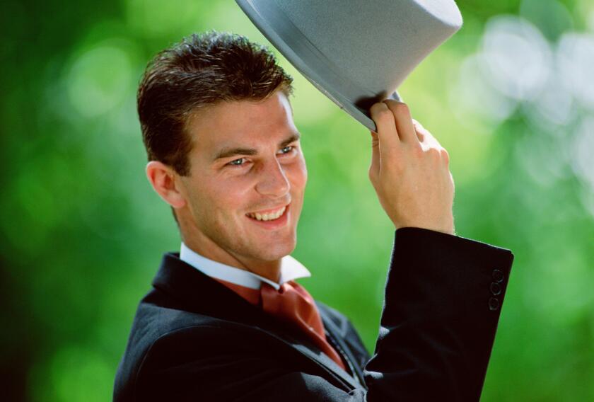 Lifestyle. Wedding. Man outdoors raising his top hat.