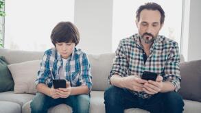 Do not leave in virtual life spend time with your relatives concept. Photo of serious kid and his bearded in checkered shirt dad holding telephones in