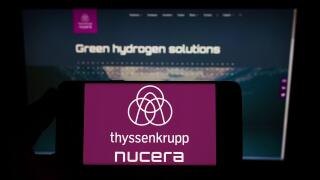 Person holding smartphone with logo of company thyssenkrupp nucera AG Co. KGaA on screen in front of website. Focus on phone display.