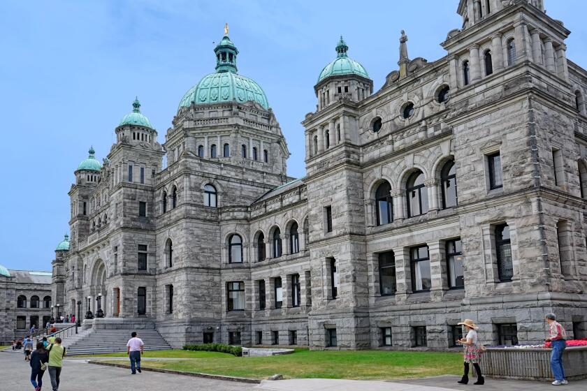 Victoria, BC, Canada -  Visitors walk past the front of the baroque style provincial parliament building of British Columbia, in the ca