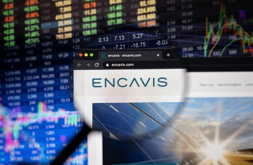 Encavis company logo on a website with blurry stock market developments in the background, seen on a computer screen through a magnifying glass