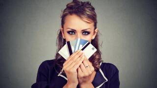 Serious woman hiding face behind many credit cards isolated on gray wall background