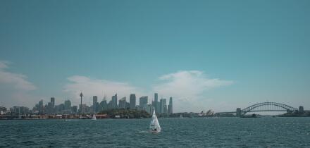 Wide angle view of the Sydney Harbour skyline featuring the CBD, Sydney Opera House, and Harbour Bridge with sailboats in the foreground.
