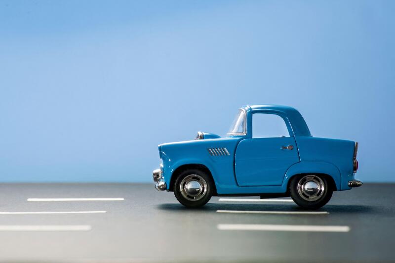 Side view of a blue toy car on a blue background and on an asphalt road.