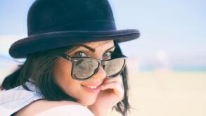 Portrait of smiling beautiful young woman in black hat. Model shooting on the beach.